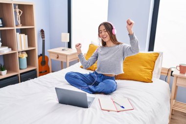 Young beautiful hispanic woman student listening to music studying on bed at bedroom