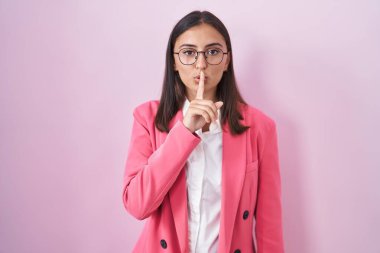 Young hispanic woman wearing business clothes and glasses asking to be quiet with finger on lips. silence and secret concept. 