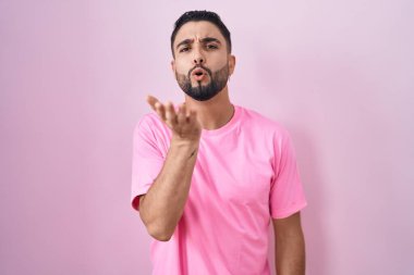 Hispanic young man standing over pink background looking at the camera blowing a kiss with hand on air being lovely and sexy. love expression. 
