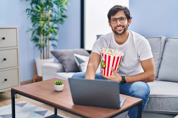 Young hispanic man watching movie eating popcorn at home