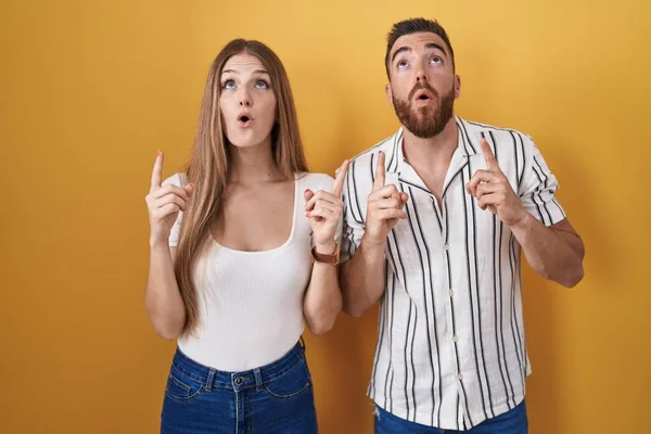 Young Couple Standing Yellow Background Amazed Surprised Looking Pointing Fingers — 图库照片