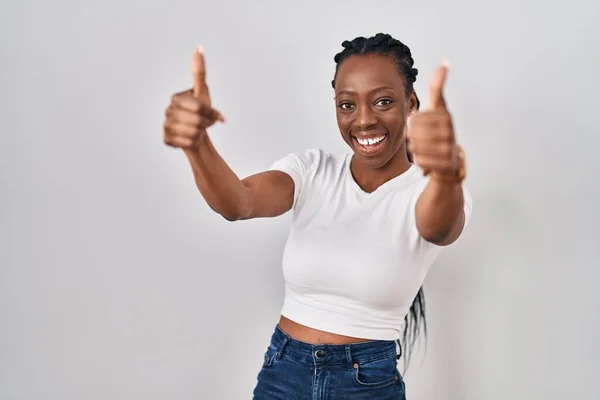 Beautiful black woman standing over isolated background approving doing positive gesture with hand, thumbs up smiling and happy for success. winner gesture.