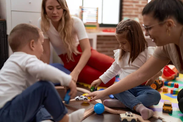 Teachers with boy and girl playing with cars toy sitting on floor at kindergarten