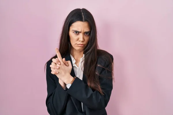 Young brunette woman wearing business style over pink background holding symbolic gun with hand gesture, playing killing shooting weapons, angry face