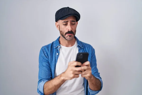 Hispanic man with beard using smartphone typing message depressed and worry for distress, crying angry and afraid. sad expression.