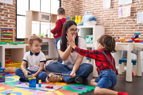 Teacher with group of boys sitting on floor high five with hands raised up at kindergarten