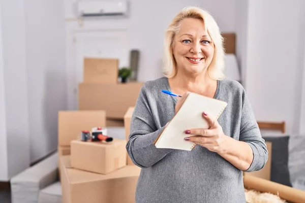 Middle Age Blonde Woman Smiling Confident Writing Notebook New Home — Stockfoto