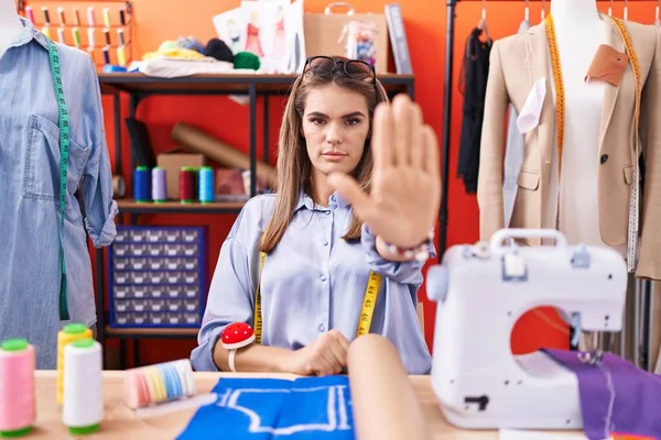 Hispanic young woman dressmaker designer at atelier room doing stop sing with palm of the hand. warning expression with negative and serious gesture on the face.