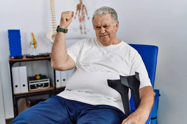 Senior Caucasian Man Physiotherapy Clinic Holding Crutches Angry Mad Raising — Stock Photo, Image