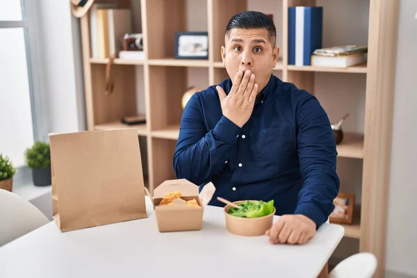 Hispanic Young Man Eating Take Away Food Covering Mouth Hand — Stockfoto