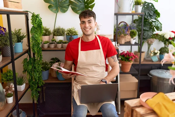 Young hispanic man florist using laptop reading book at flower shop