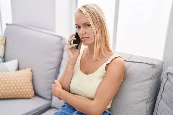 Young Blonde Woman Talking Smartphone Serious Expression Home — Stockfoto