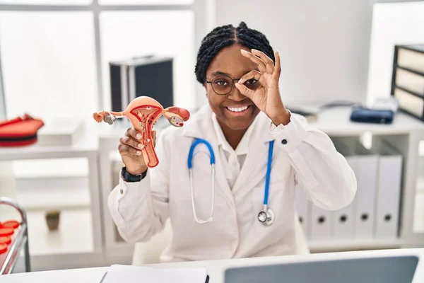 African american doctor woman holding anatomical model of female genital organ smiling happy doing ok sign with hand on eye looking through fingers