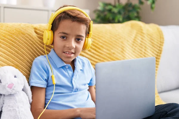 可爱的他的惊慌失措的男孩坐在家里沙发上 用笔记本电脑和耳机 — 图库照片