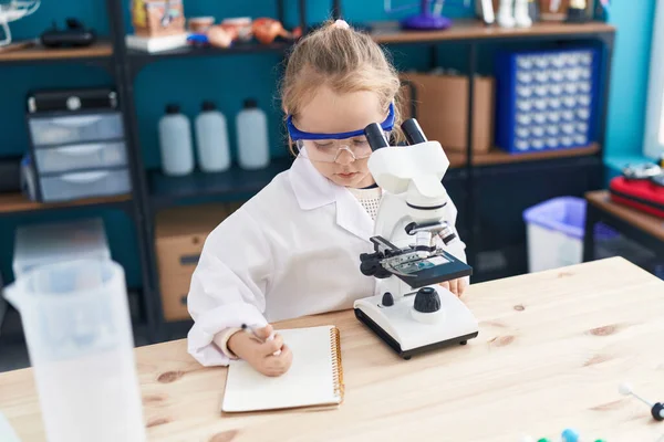 Adorable Blonde Girl Student Using Microscope Writing Notebook Laboratory Classroom — Photo