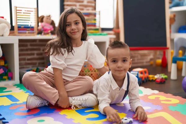 弟と妹は自信を持って笑顔で幼稚園の床に座って — ストック写真