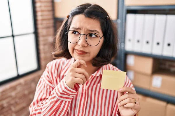 Young Hispanic Woman Holding Paper Reminder Office Serious Face Thinking — Stok fotoğraf