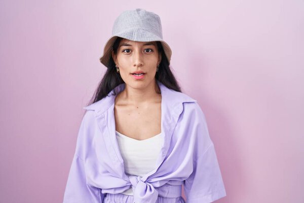Молодая латиноамериканка, стоящая на розовом фоне в шляпе, выглядящая сонной и уставшей, уставшая от усталости и похмелья, ленивые глаза по утрам. 