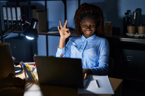 African woman working at the office at night smiling positive doing ok sign with hand and fingers. successful expression.