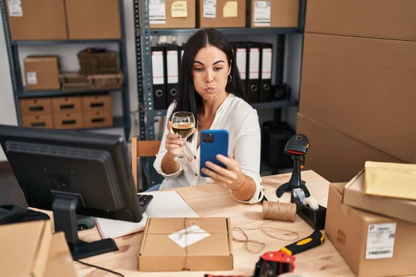 Young Hispanic Woman Working Drinking Wine Using Smartphone Puffing Cheeks — Fotografia de Stock