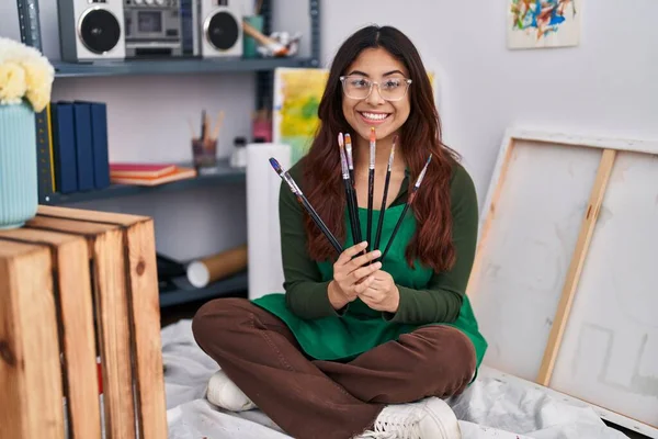 Young Hispanic Woman Artist Holding Paintbrushes Sitting Floor Art Studio — Stockfoto