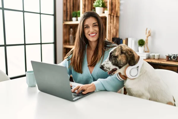 stock image Young woman using laptop sitting on table with dog wearing headphones at home