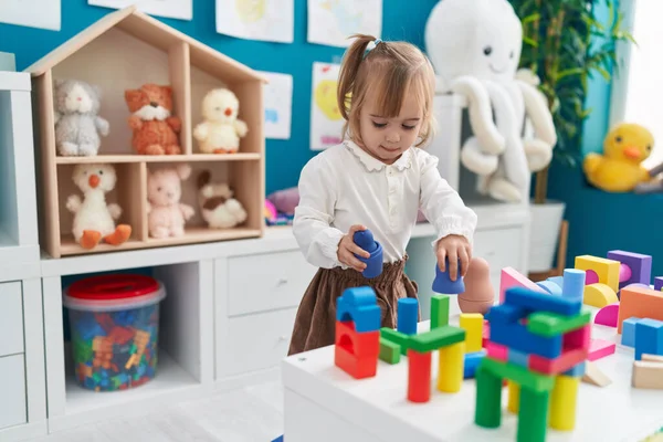 Adorable blonde girl playing with construction blocks standing at kindergarten