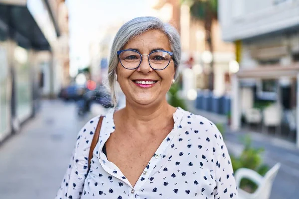 Orta yaşlı bir kadın sokakta kendine güvenerek gülümsüyor.