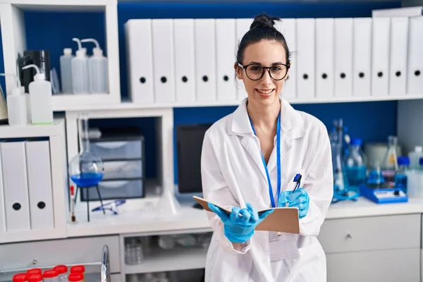 Young caucasian woman scientist smiling confident writing on notebook at laboratory