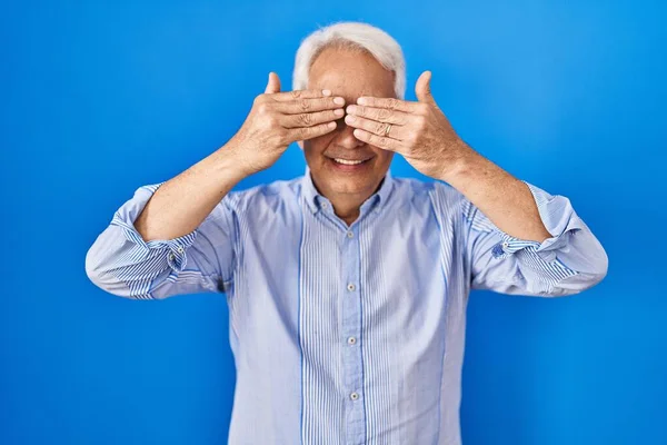 Hispanic senior man wearing glasses covering eyes with hands smiling cheerful and funny. blind concept.