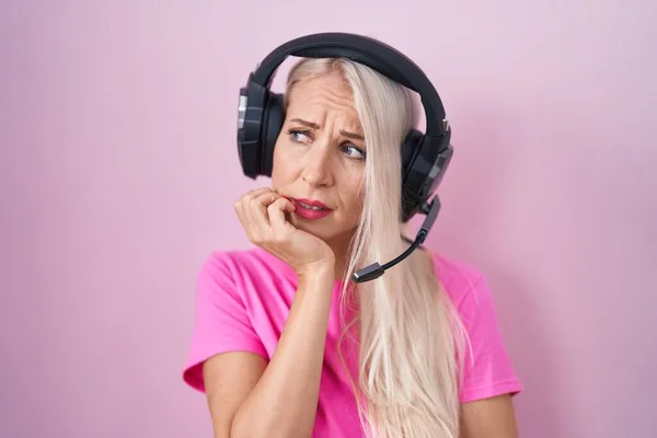 Caucasian woman listening to music using headphones looking stressed and nervous with hands on mouth biting nails. anxiety problem.