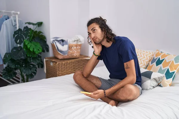 Young Hispanic Man Using Smartphone Worried Expression Bedroom — Fotografia de Stock