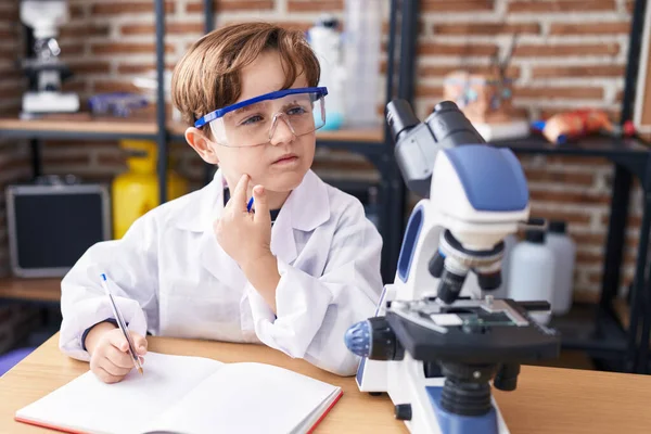 Not defterine laboratuvar sınıfında şüpheyle yazı yazan sevimli İspanyol çocuk.