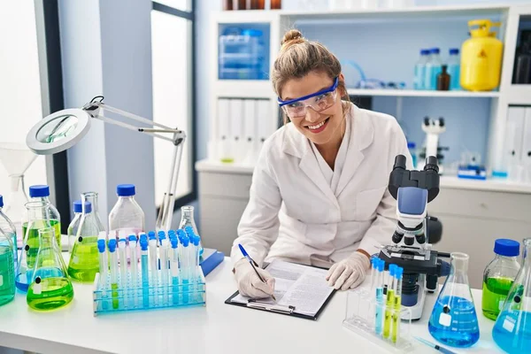 Laboratuvarda panoya yazan bilim adamı üniforması giyen genç sarışın kadın.