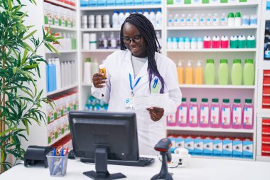Afrika kökenli Amerikalı kadın eczacı elinde ilaç şişesiyle eczanede reçete okuyor.