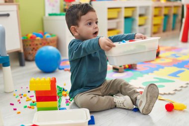 Adorable hispanic boy playing with construction blocks sitting on floor at kindergarten