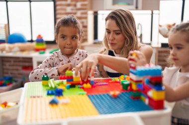 Teacher with girls playing with construction blocks sitting on table at kindergarten