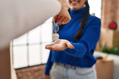 Young hispanic woman smiling confident reciving key of new house at new home