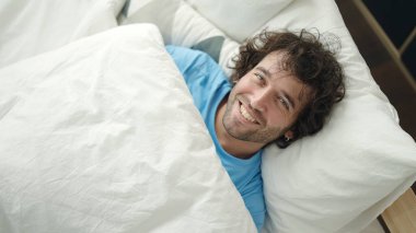 Genç İspanyol adam yatakta kendinden emin bir şekilde gülümsüyor.