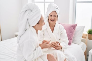 Mother and daughter wearing bathrobe drinking coffee at bedroom