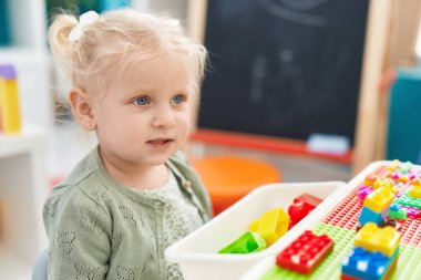 Adorable blonde girl playing with construction blocks sitting on table at kindergarten