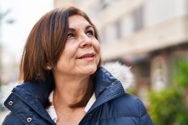 Orta yaşlı bir kadın sokakta kendinden emin bir şekilde gülümsüyor.