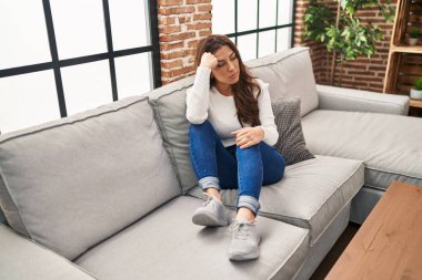 Evdeki kanepede oturan ciddi ifadeli İspanyol genç kadın.