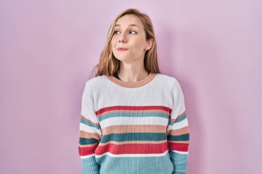 Pembe arka planda duran genç sarışın kadın gülümsüyor, yan tarafa bakıyor ve düşünüyor.. 