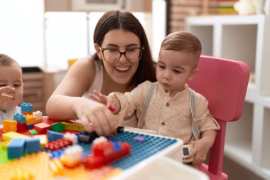 Anaokulunda masada oturan öğretmen ve anaokulu öğrencisi inşaat bloklarıyla oynuyor.