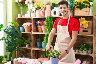 Young hispanic man florist cutting plants at flower shop
