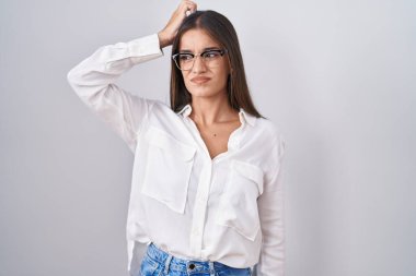 Young brunette woman wearing glasses confuse and wondering about question. uncertain with doubt, thinking with hand on head. pensive concept. 