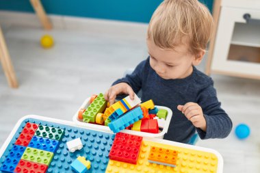 Anaokulundaki masada oturan sevimli sarışın çocuk inşaat bloklarıyla oynuyor.