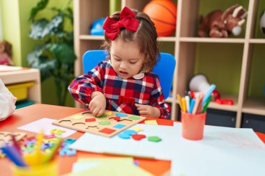 Anaokulunda yerde oturmuş matematik oyunu oynayan sevimli sarışın çocuk.