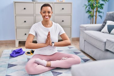 Afro-Amerikalı kadın gülümseyerek evde yoga eğitimi alıyor.